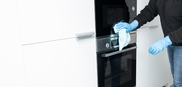 Cropped shot of a woman cleaning a modern stainless steel oven door